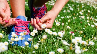 Frau bindet Sportschuhe auf einer Wiese zu.