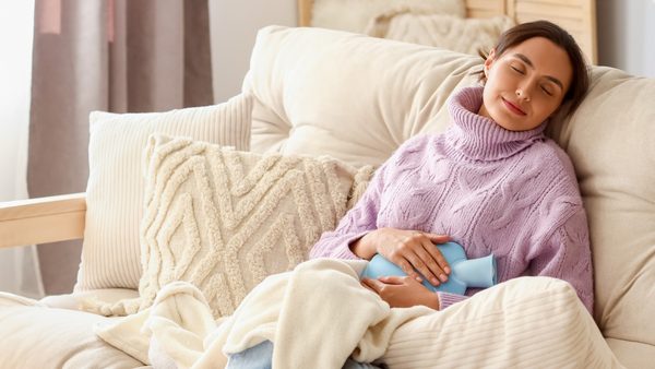 Junge Frau mit einer Wärmflasche auf dem Sofa - Zur Linderung von Blasenentzündungen