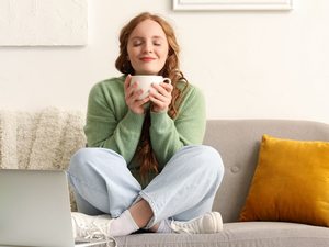 Entspannte Frau mit einer Tasse Tee auf dem Sofa – Stressabbau kann helfen, Blasenentzündungen durch Stress zu vermeiden.