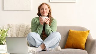 Entspannte Frau mit einer Tasse Tee auf dem Sofa – Stressabbau kann helfen, Blasenentzündungen durch Stress zu vermeiden.