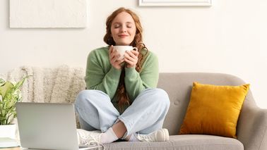 Entspannte Frau mit einer Tasse Tee auf dem Sofa – Stressabbau kann helfen, Blasenentzündungen durch Stress zu vermeiden.