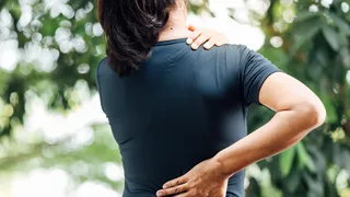 Frau fasst sich an die Schulter und den unteren Rücken.