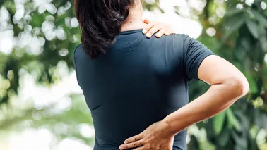 Frau fasst sich an die Schulter und den unteren Rücken.