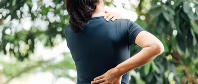 Frau fasst sich an die Schulter und den unteren Rücken.