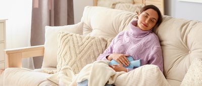 Entspannte Frau mit Wärmflasche auf dem Sofa – Wärme kann bei einer Blasenentzündung helfen.