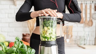 Sportliche Frau bereitet grünen Smoothie zu