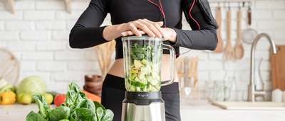 Sportliche Frau bereitet grünen Smoothie zu