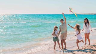 Eltern mit zwei Kindern spielen fröhlich am Meer und lassen einen Drachen steigen.