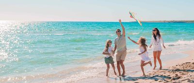 Eltern mit zwei Kindern spielen fröhlich am Meer und lassen einen Drachen steigen.