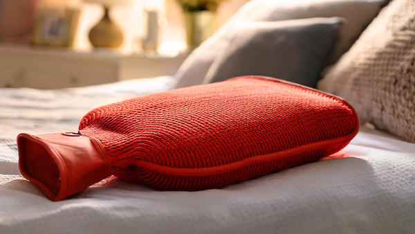 Wärmflasche auf dem Bett kann Menstruationsbeschwerden lindern.