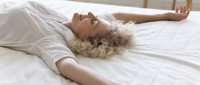 Frau liegt mit ausgestreckten Armen auf dem Bett – Symbol für entspannenden Schlafkomfort