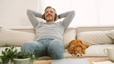 Älterer Mann sitzt mit Hund auf Couch und hört Musik zum Entspannen.