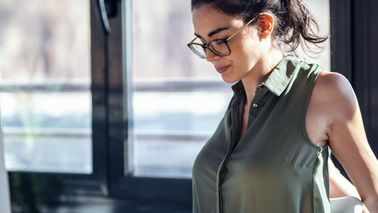 Frau sitzt am Schreibtisch und dehnt ihren Rücken.