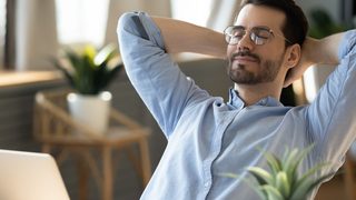 Mann sitzt mit geschlossenen Augen am Schreibtisch und legt sich zurück - Entspannung bei nervösem Magen