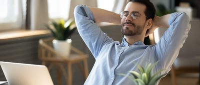 Mann sitzt mit geschlossenen Augen am Schreibtisch und legt sich zurück - Entspannung bei nervösem Magen