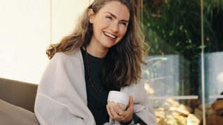 Ältere fröhliche Frau sitzt mit Tasse auf Terrasse