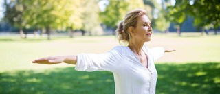 Ältere Frau in der Natur streckt die Arme aus.