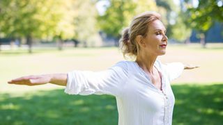 Ältere Frau in der Natur streckt die Arme aus.