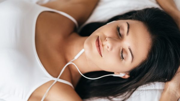 Frau liegt im Bett und hört zum Einschlafen Musik