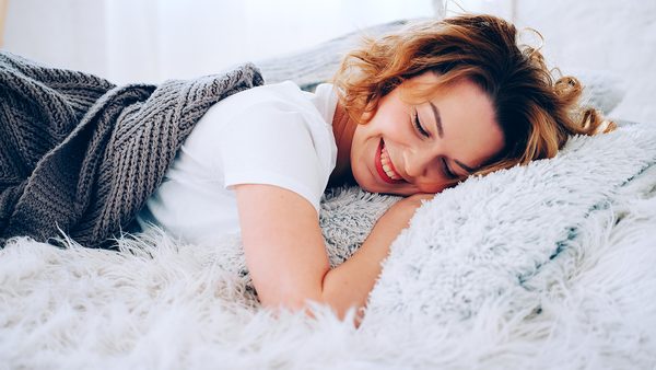 Frau liegt lachend im Bett - Symbol für erholsame Schlafphasen