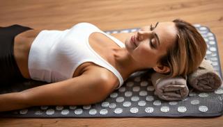 Entspannte Person liegt auf einer Akupressurmatte mit Handtuchrollen unter dem Nacken – mögliche Anwendung bei Neuralgie.