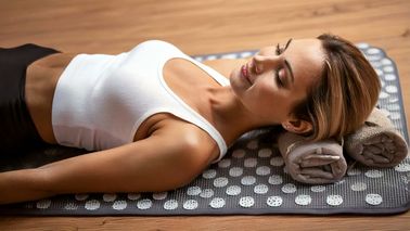 Entspannte Person liegt auf einer Akupressurmatte mit Handtuchrollen unter dem Nacken – mögliche Anwendung bei Neuralgie.