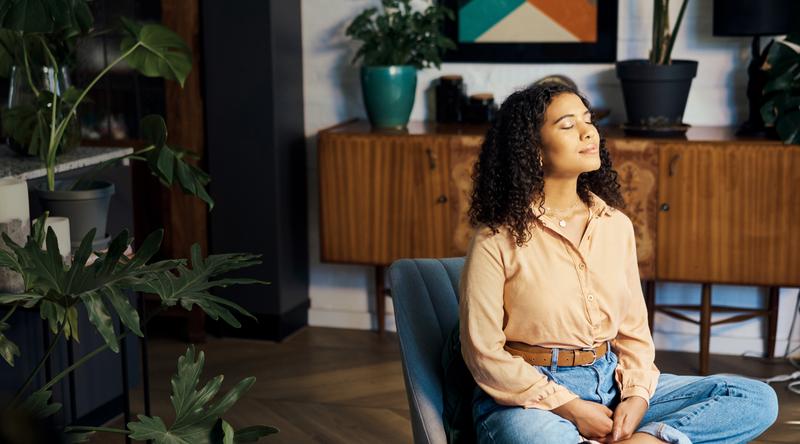 Frau sitzt im Schneidersitz auf einem Stuhl im Wohnzimmer