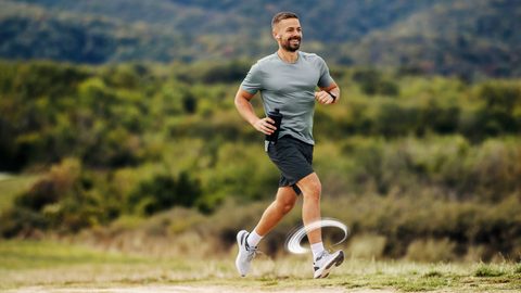 Lächelnder Mann joggt mit Flasche in der Hand