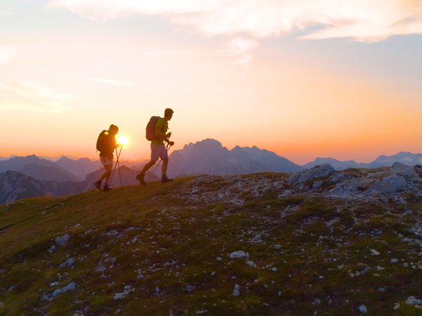 Zwei Personen wandern in den Bergen bei Sonnenuntergang – moderate Bewegung unterstützt Herz und Kreislauf