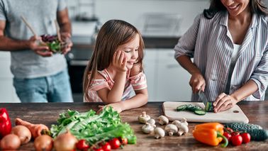 Mädchen schaut ihrer Mutter beim kochen zu.