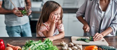 Mädchen schaut ihrer Mutter beim kochen zu.