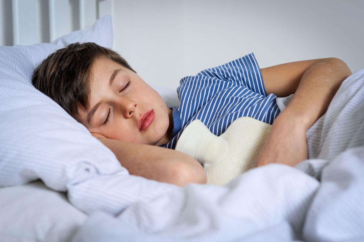 Junge liegt mit einer Wärmflasche im Bett