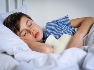 Junge liegt mit einer Wärmflasche im Bett