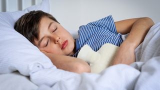 Junge liegt mit einer Wärmflasche im Bett