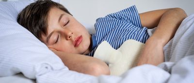 Junge liegt mit einer Wärmflasche im Bett