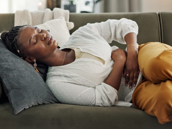 Frau mit Unterleibsschmerzen auf der Couch.