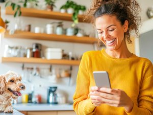 Frau in Küche mit Smartphone und Hund – Symbol für zyklusbasierte Ernährung und Wohlbefinden.