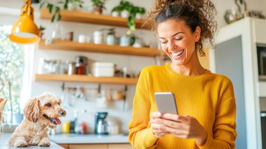 Frau in Küche mit Smartphone und Hund – Symbol für zyklusbasierte Ernährung und Wohlbefinden.