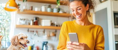 Frau in Küche mit Smartphone und Hund – Symbol für zyklusbasierte Ernährung und Wohlbefinden.