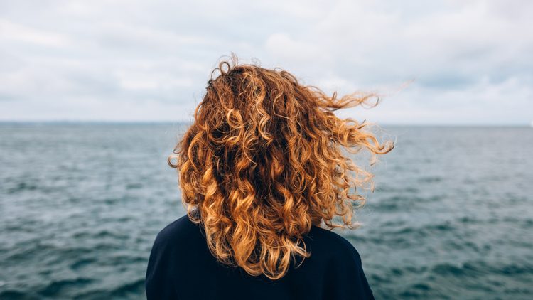 Frau mit lockigem Haar blickt auf das Meer