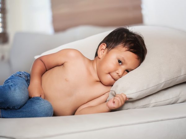 Kleiner Junge liegt auf dem Bett und hält sich den Bauch fest