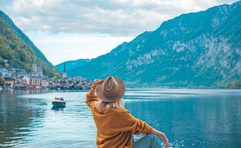 Frau sitzt entspannt am See und genießt die Aussicht auf das Wasser und die Berge