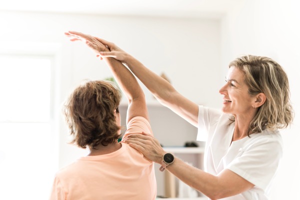 Therapeutin macht mit älterer Patientin Physiotherapie