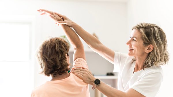 Therapeutin macht mit älterer Patientin Physiotherapie