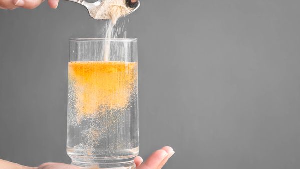 In einem Glas Wasser wird ein orangenes Pulver aufgelöst.