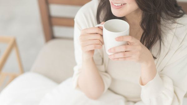 Frau trinkt im Bett eine Tasse Tee bei Blasenentzündung.