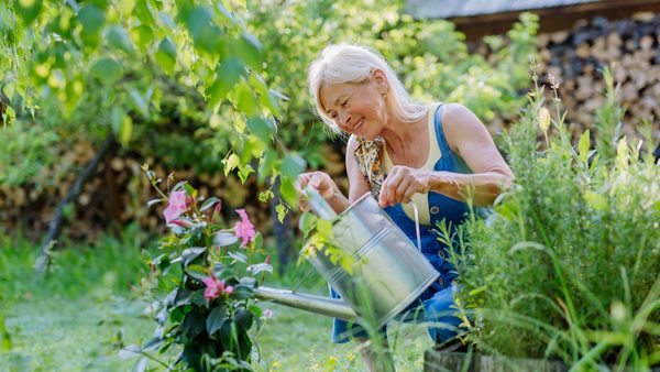 Ältere Frau gießt sichtlich glücklich die Blumen im Garten