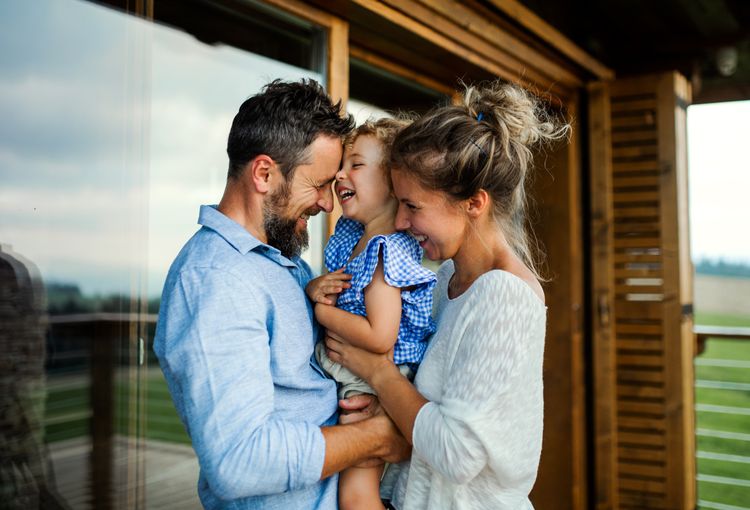 Mutter und Vater halten ihre Tochter auf dem Arm und lachen gemeinsam