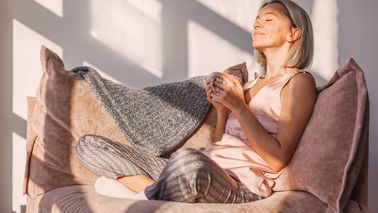 Frau entspannt mit einer Tasse Tee auf einer Couch.