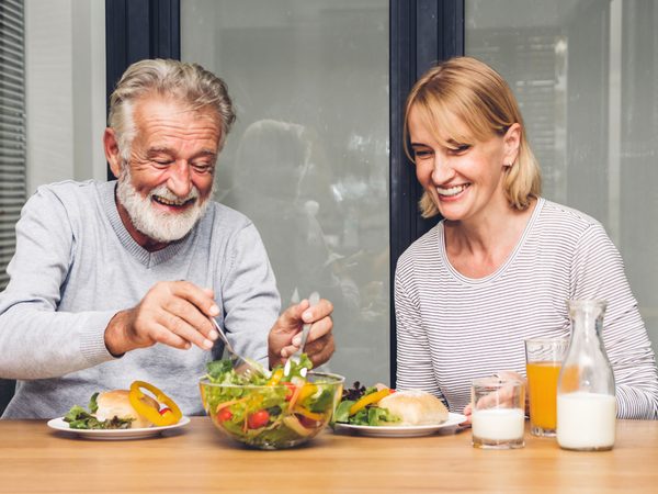Lächelndes Paar beim Essen von Salat, Saft und Milch – motivierendes Symbol für alltagstaugliche, magenfreundliche Essgewohnheiten.